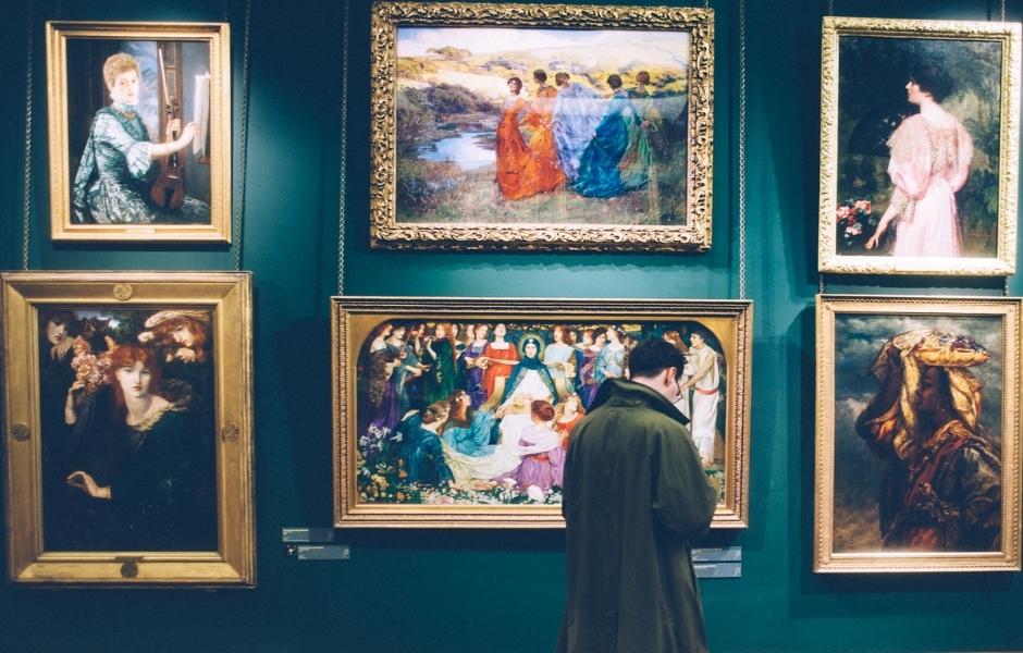 Visitor examining framed paintings on a gallery wall, representing the media assets institutions manage with TMS Media Studio