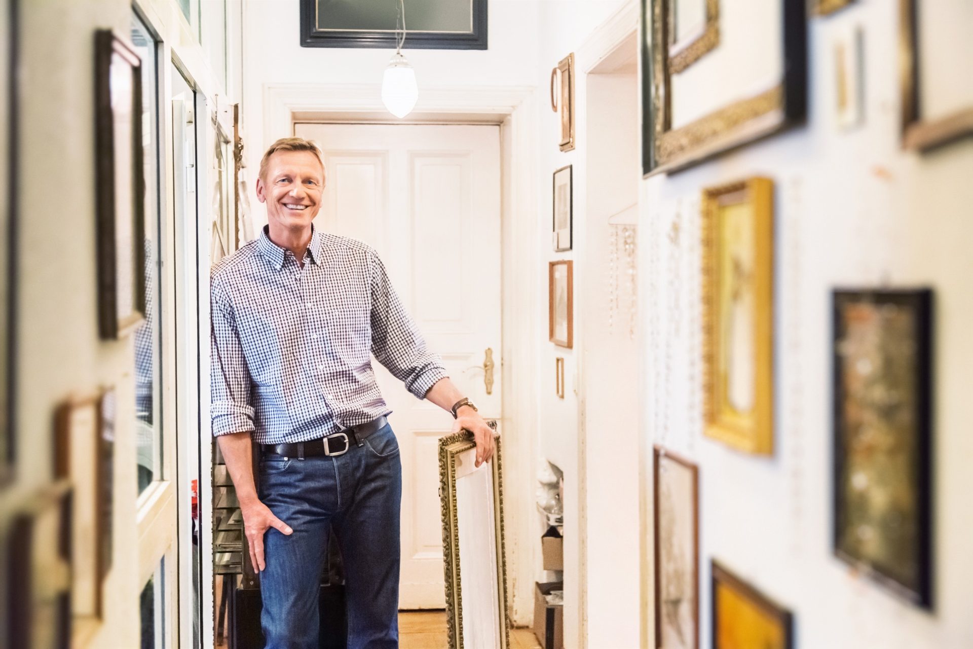 art collector in his home posing with his art collection that is hung salon style in a hallway.