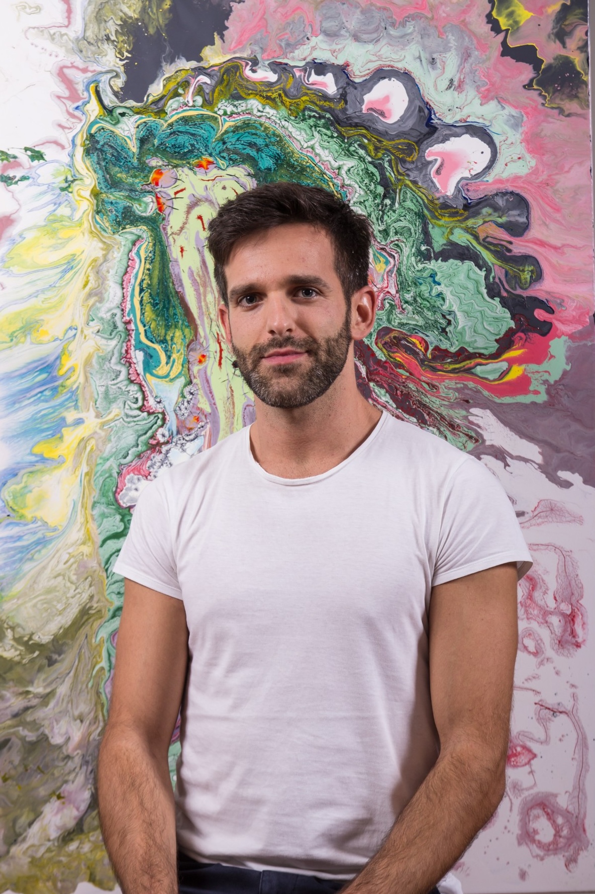 young male artist posing in front of his colorful abstract painting.