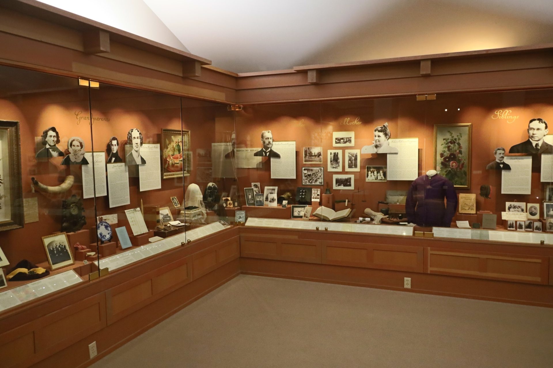 A heritage institution display combining photographs, documents, objects, and garments in wall-mounted cases, representing the diverse media centralised within a digital asset management system