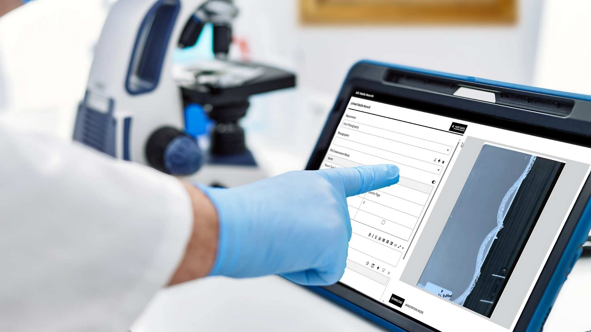 A conservator in blue gloves using TMS Conservation Studio on a tablet beside a microscope, accessing linked media records and technical imaging in a conservation lab