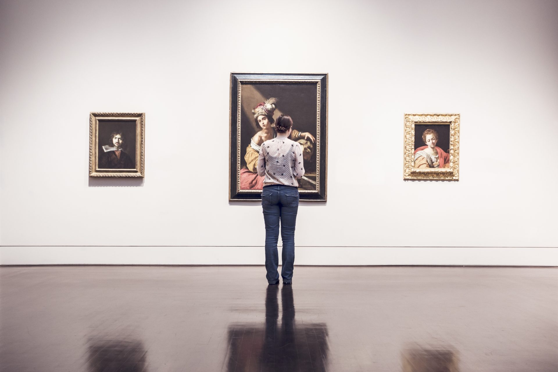 museum visitor looking at three paintings in an exhibition.