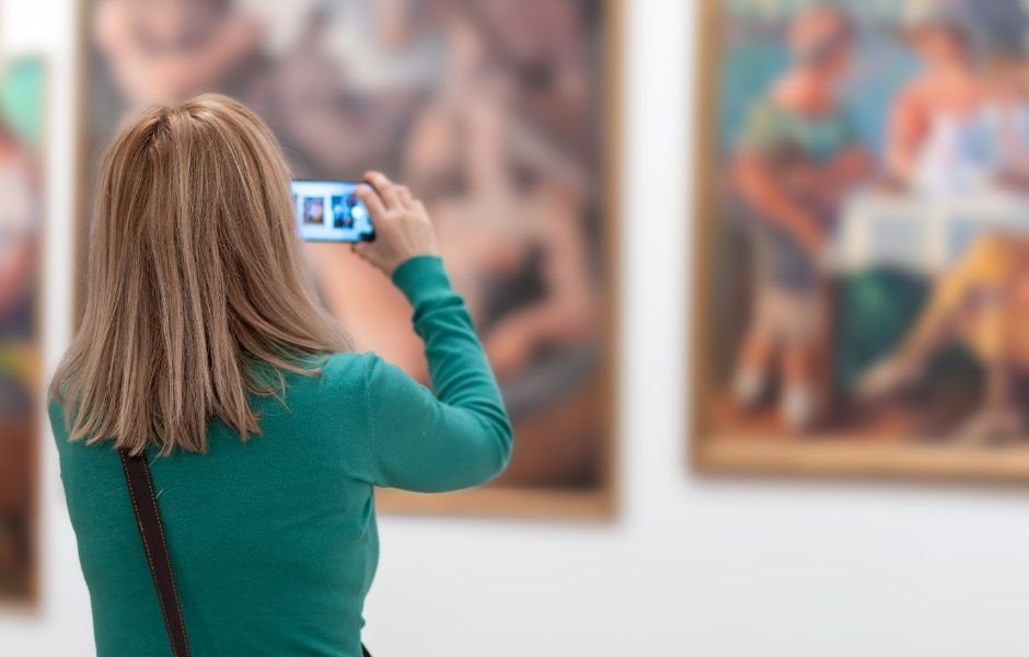 Visitor photographing paintings in a gallery, representing the media assets institutions capture and manage with Gallery Systems.