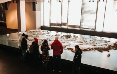 A group of visitors standing before a large-scale topographic model in an exhibition space, reflecting shared discovery across institutions